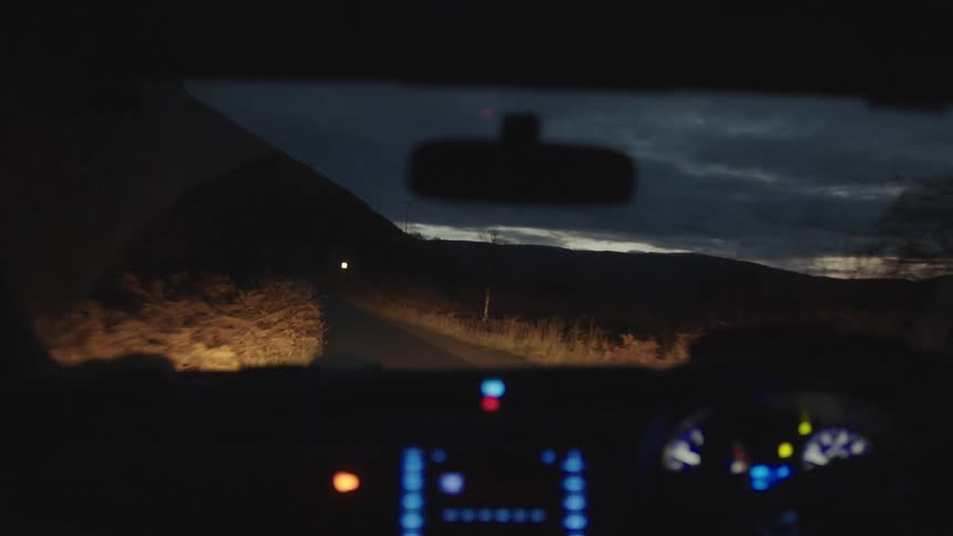 Vehicle illuminating the road with headlights drives on a country road at dusk
