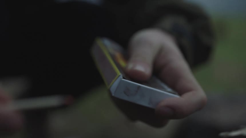 A man lights a match from a box of matches while standing outside