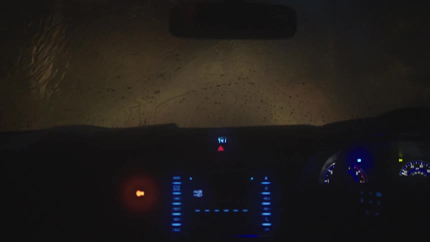 Vehicle illuminating the road with headlights drives on a country road while it rains at night