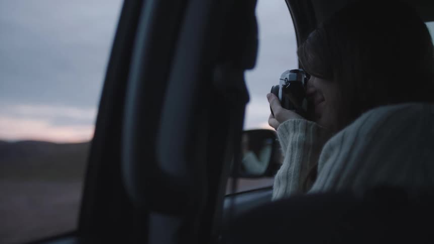 A woman takes a photo of the passing landscape as she is driven in a car
