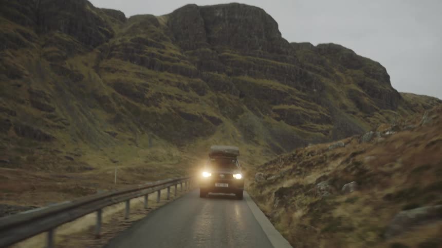 Car drives down winding mountain road at night past grassy rocks