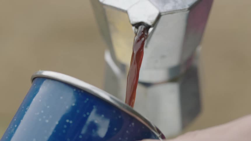 A person pour coffee from an espresso maker to a coffee mug