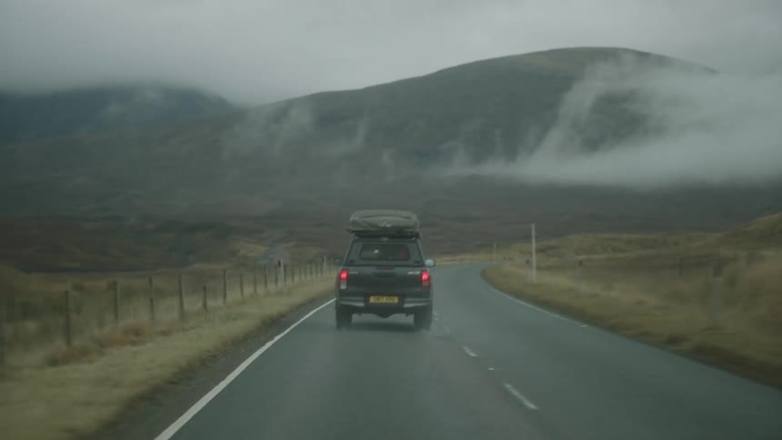 Clouds hang low in front of hills as a truck travels on an empty road
