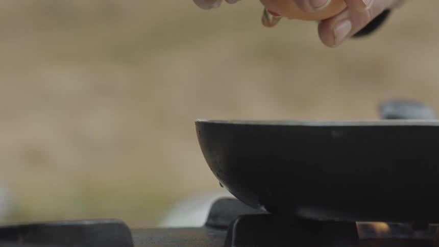 Mans hands crack an egg into a pan