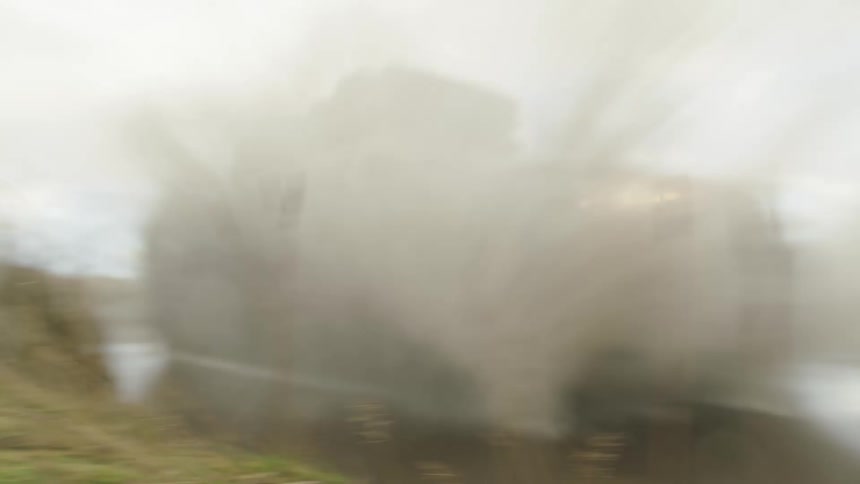 A sport utility vehicle drives through a large puddle at high speed and sends dirty water flying