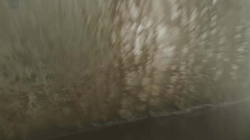 Silver suv driving through a puddle of water and splashing it at daytime next to a slope of grass