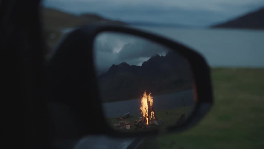 The reflection of a campfire in a vehicles rearview mirror