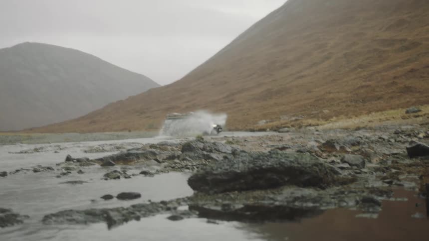 A sport vehicle drives through a mountainside shallow pond