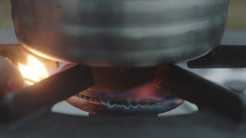 A hand takes a lit match to lit the gas for a stove top burner