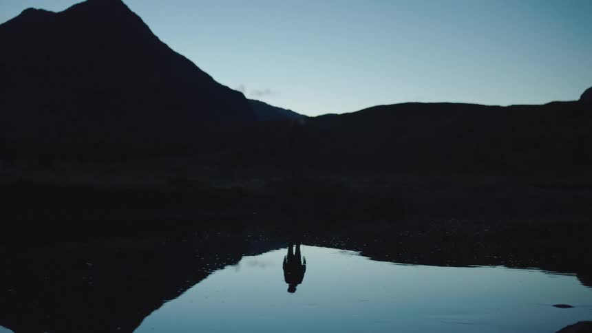 A mans silhouette is reflected in a clear lake at a canyon