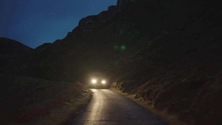 A car drives on a road at night next to a hillside