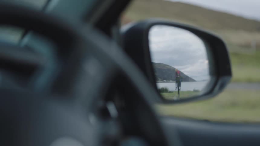 A couple walks towards a car from the waters edge reflected in the side view mirror