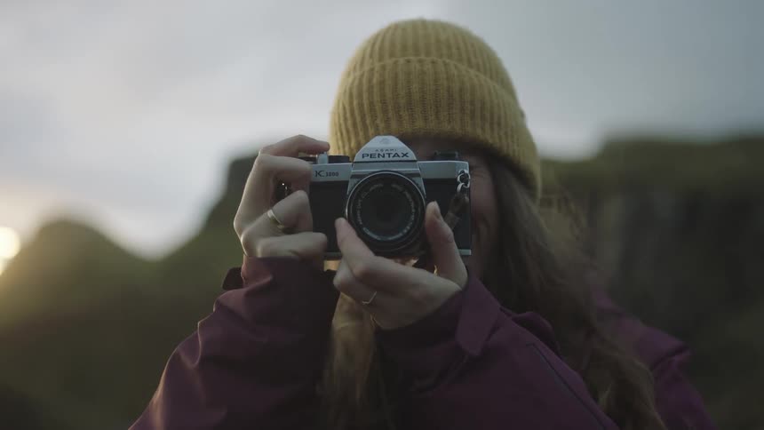 A female photographer takes a photograph while standing outdoors on a cold and windy day