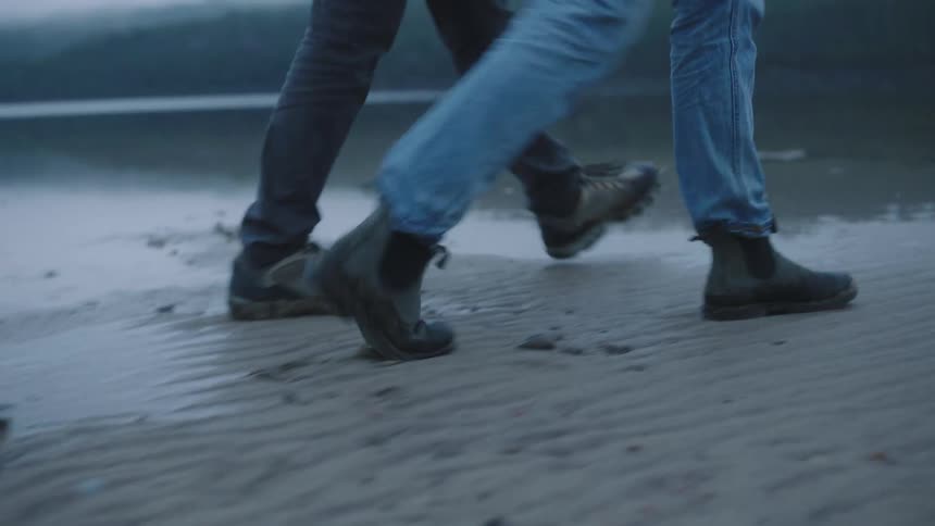 Man and woman with jeans and boots walk around the lake on a cloudy day