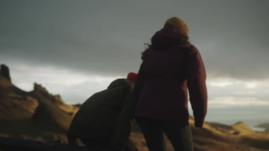 A man grabs his girlfriends hand as they walk through a canyon and go sit near their vehicle