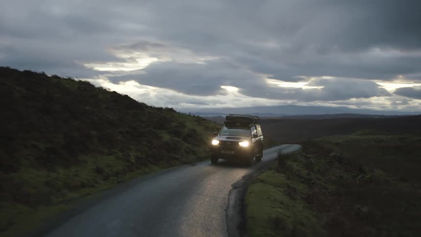 Car driving down a one lane highway at dusk out in the wilderness