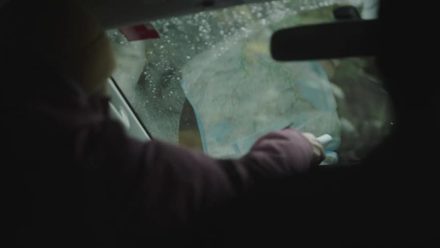 A passenger in a moving car reaches for a map on the dashboard