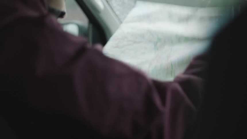Woman wearing coat unfolds map while sitting in passenger side of moving vehicle