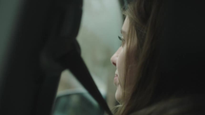 A woman is a passenger in a moving car looking through the window