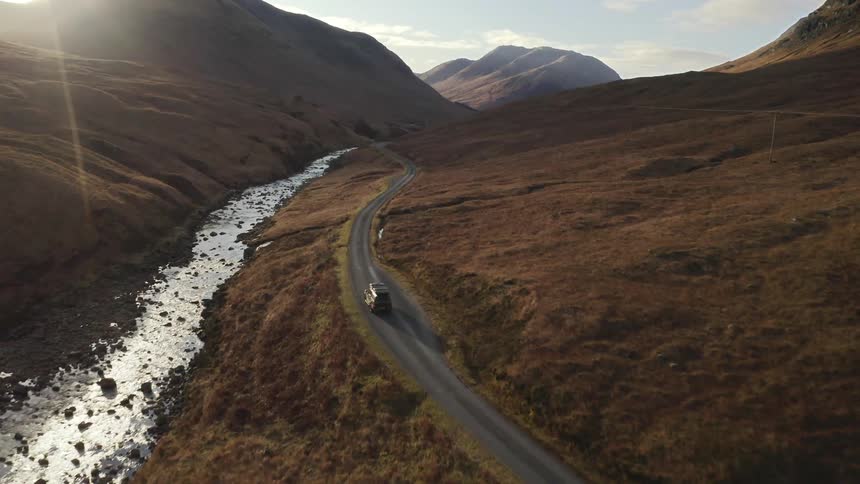 A truck drives along a remote road located next to a river surrounded by hills