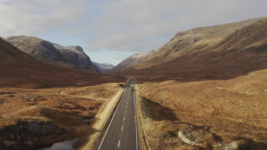 A person in a vehicle traveling down a desolate road near the mountains