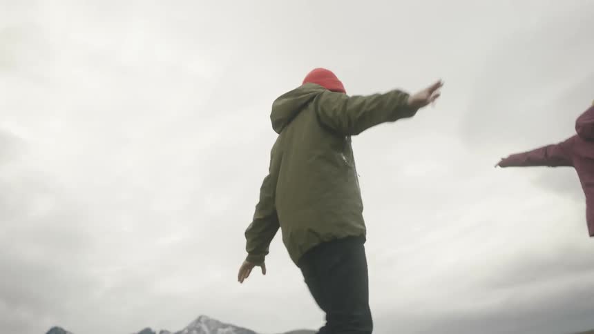 Man and woman walking on a narrow rock wall at day time next to a mountain range