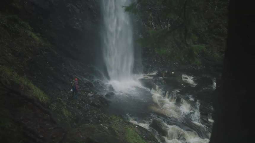 A waterfall with two people standing at the bottom of it with arms raised in celebration