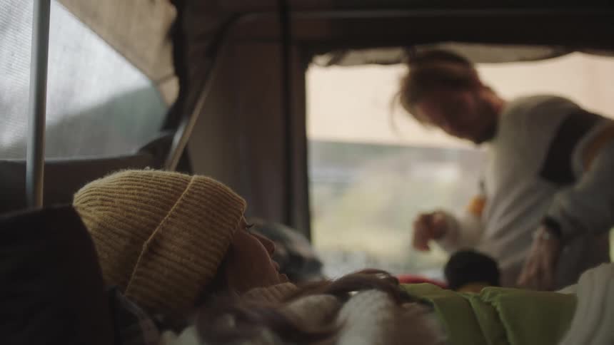 Woman laying down inside of a camping tent at day time next to a man sorting clothing at the opening