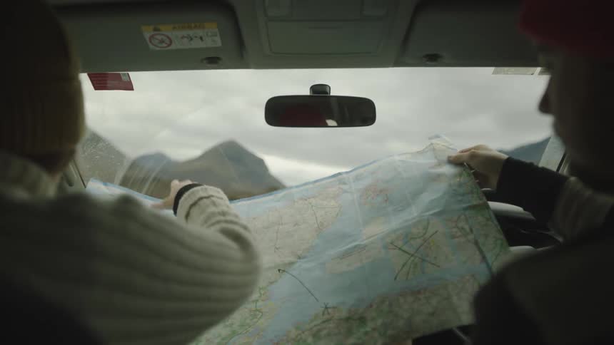 Two people sit in a vehicle and open a large map to look at