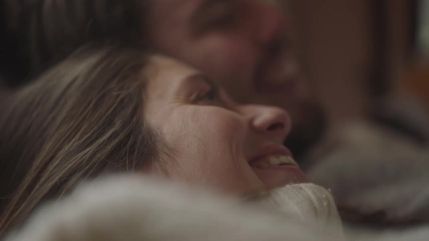 A man leans over and kisses a woman on the head as they lie together