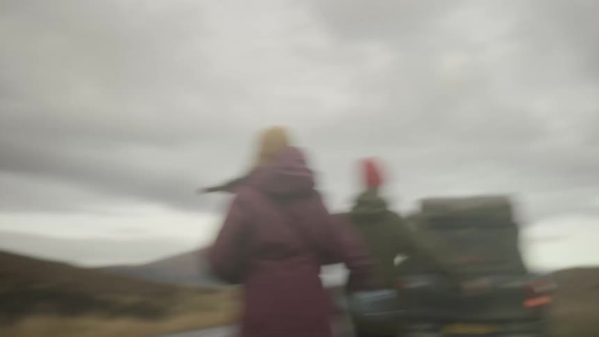 A man and woman run to their sport utility vehicle parked on the side of a rural highway