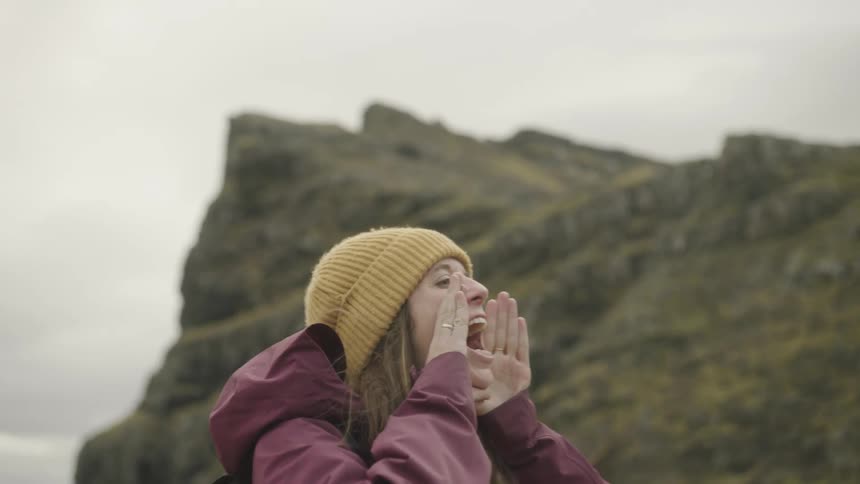 A woman holds her hands to her mouth and screams into the distance while hiking in a canyon