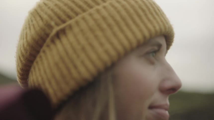 Woman stands with hair blowing in the wind looking off into the distance with small smile on her face