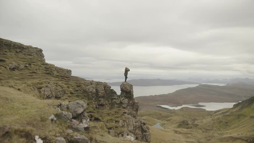 A person in a red hat stands on top of a rock formation in a canyon and waves their arms around