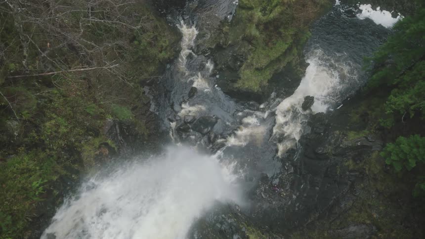 Waterfall falling down a river in a forest between two slopes covered in moss and vegetation