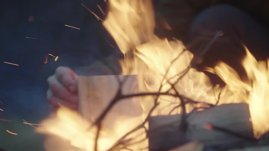 Hand placing a fresh cut log in the evening into a burning fire