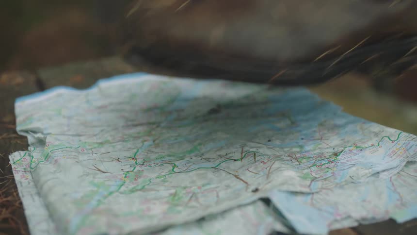 A pair of boots are placed atop a tattered map on a wooden bench
