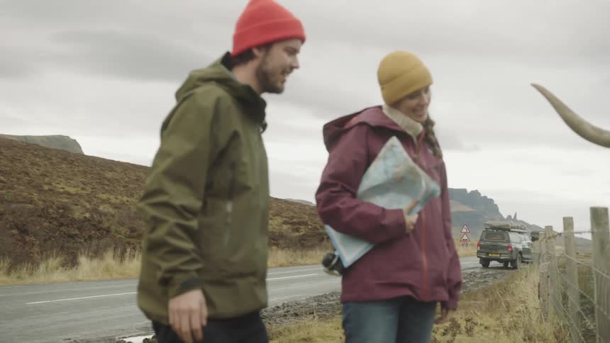 Man and a woman petting and feeding highland cattle at the side of a road from behind a wired fence