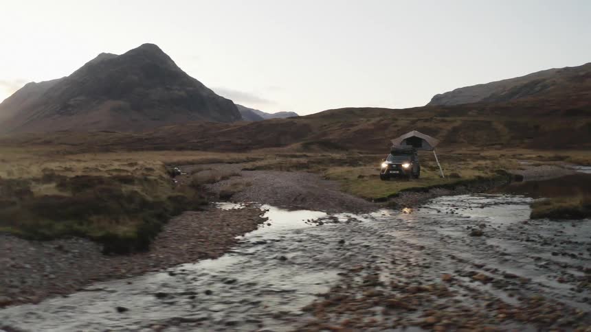 People sit around camp near vehicle with popup tent parked near lake in valley