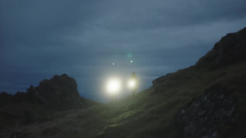 Two people are using flashlights to walk on a hill at night