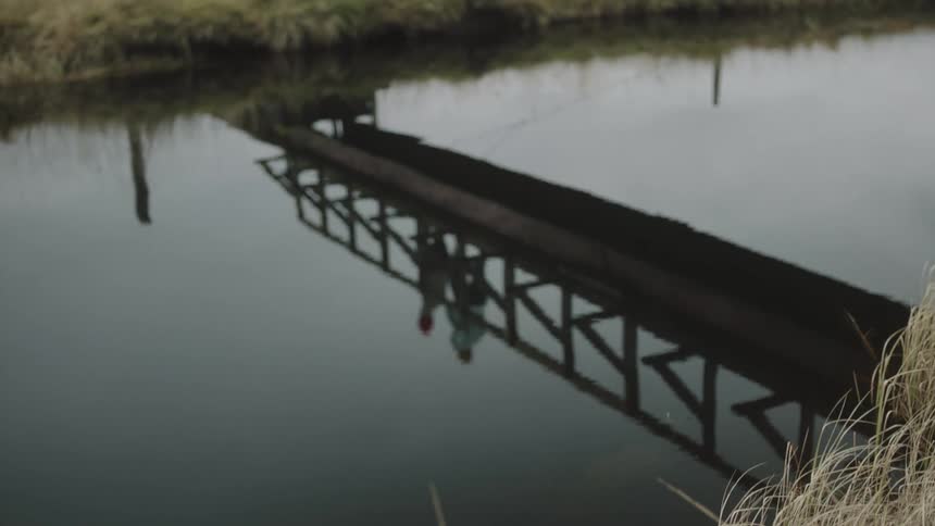 Two people are running on a bridge with the reflection on water at dusk