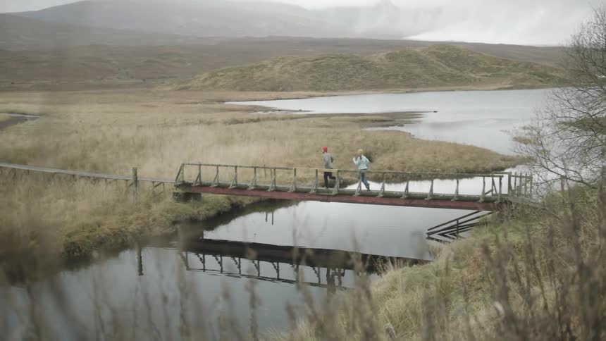Two people are running across a bridge with water underneath it