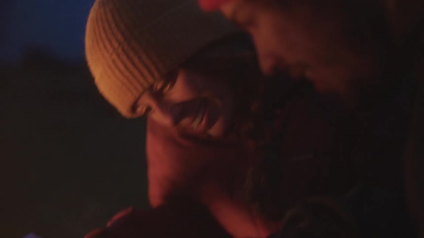 A man and a woman sit in front of a fire reading a map talking and laughing