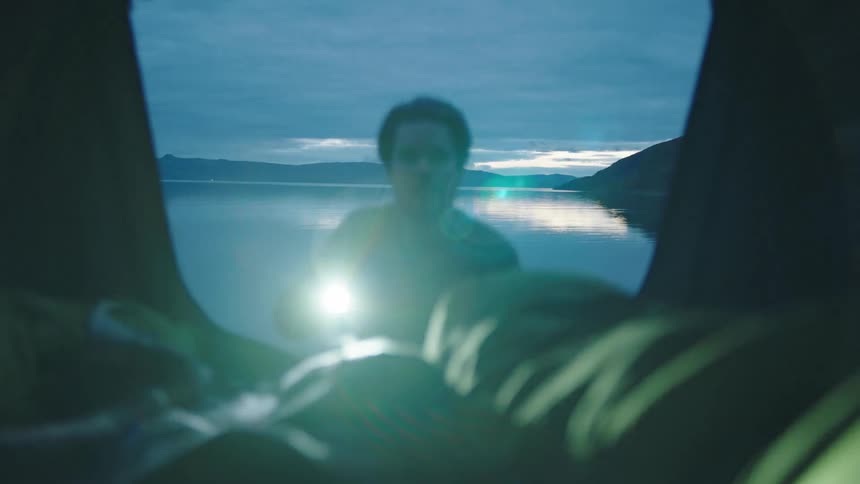 A man walks from a beach into a camper using a flashlight