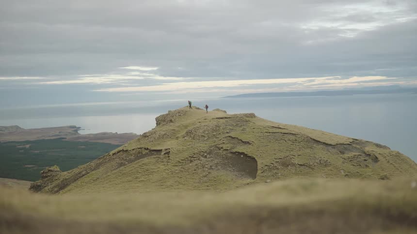 Two people hiking reach the top of a hill under a cloudy sky