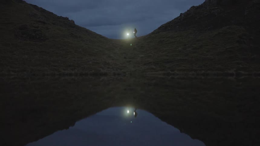 Two people standing nears hills using a flashlight that is reflecting in water