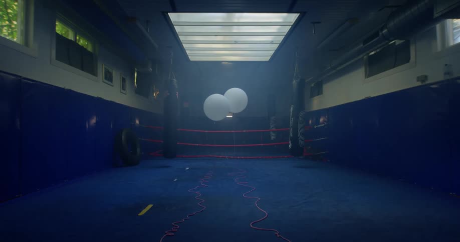 Two white balloons tied to strings on the ground inside of an empty boxing ring