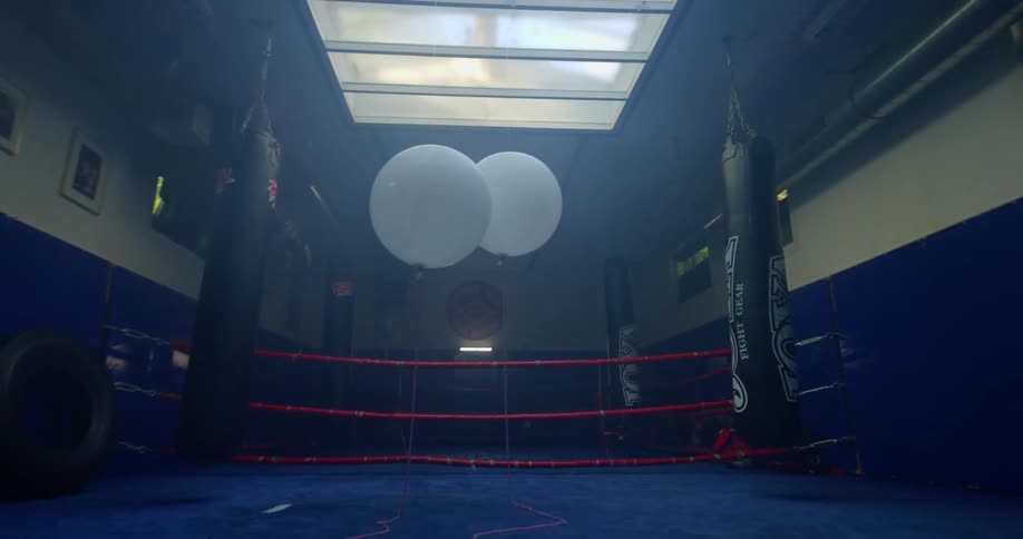 A pair of white balloons floating inside a gym between black punching bags