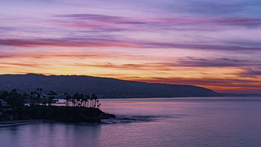 Red sky horizon at sunset above the coast of a shore next to land with palm trees