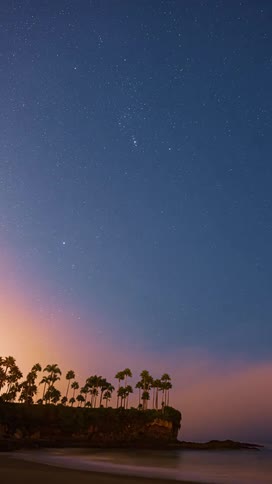 Stars fade in the night sky over a beach and cliff as dusk turns to dawn